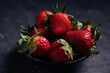 © Ramon Lopez/ADDICTIVE STOCK - Closeup of delectable juicy ripe strawberries with green leaves arranged in black ceramic bowl on dark background