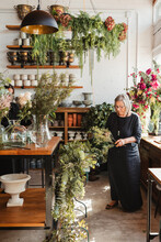 Professional Adult Female Florist Choosing Green Decorative Plants For Composition While Working With Colleague In Cozy Floristry Studio