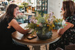 © Raquel Arocena/ADDICTIVE STOCK - Side view of female owner of stylish floristry salon discussing details of order with customer while sitting together at table with laptop in a happy attitude