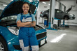 © Svitlana - Keep your auto moving. Young african american woman, professional female mechanic smiling at camera, leaning on a car in auto repair shop