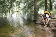 © Sergio Victor Vega/ADDICTIVE STOCK - young man hiking with yellow backpack and hat tying his shoelaces on the shore of a tree-filled lake