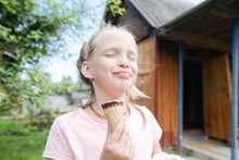 Portrait Of Happy Blond Girl With Eyes Closed Enjoying Ice Cream With In Garden