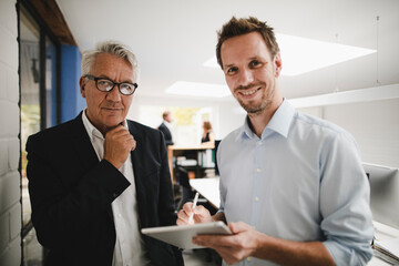 Two successful businessmen standing in office, using digital tablet