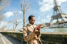Woman Using Smart Phone On Bridge With Eiffel Tower In Background Against Sky, Paris, France