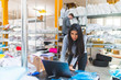 © Westend61 - Woman using laptop with businessman in background in a warehouse