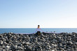 © Westend61 - Woman with artificial long hands sitting on pebbles at beach against clear sky