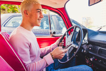 Smiling Teenage Boy Sitting In Vintage Car With Smartphone