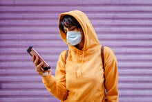 Portrait Of Young Woman With Yellow Hoodie And Protective Mask In Front Of Purple Background