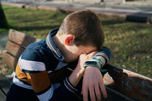 Child On A Bench Covers His Face With His Arm And Is Crying