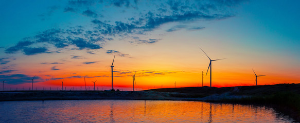 Wall Mural - silhouettes of wind generators power plant on lake at sunrise