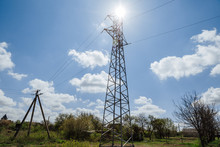 A Metal High-voltage Tower Against A Blue Sky With White Clouds Towering Above The Trees. Power Supply