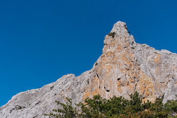 High mountain against a clear blue sky. At the foot of the mountain trees sprout