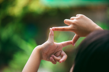 A little girl is making her hand gestures a camera symbol to aim at a target like she is actually using a camera.