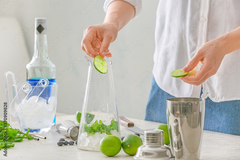 Woman making tasty mojito cocktail at table