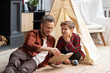 © deniskomarov - Father and son with book sitting on floor at home