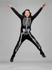 Wall Mural - halloween, holiday and childhood concept - smiling boy in black costume with skeleton bones jumping over grey background