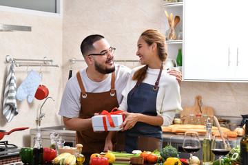 Asian woman feeling happy when surprised with a gift from boyfriend while cooking in kitchen and making healthy food together