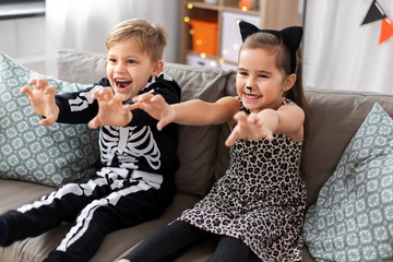 Wall Mural - halloween, holiday and childhood concept - smiling little boy and girl in party costumes having fun at home