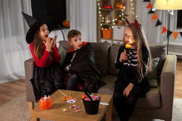 Sticker - halloween, holiday and childhood concept - smiling boy and girls in party costumes playing with flashlight and scaring each other at home