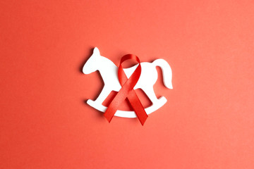 Wall Mural - Red ribbon as symbol of aids awareness with children toy on red background.