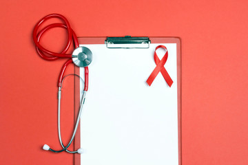 Wall Mural - Empty medical folder with red ribbon as symbol of aids awareness and stethoscope on red background.