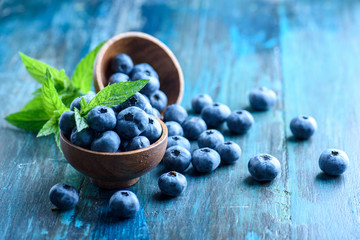 Bowl of fresh blueberries on blue rustic wooden table closeup.