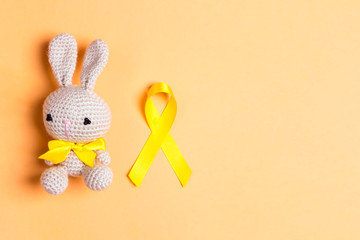 Wall Mural - Childhood Cancer Awareness Golden Ribbon with toy bunny on yellow background. Copy space for text.