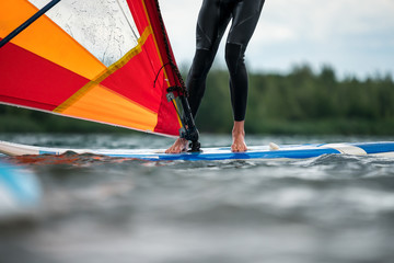 Man in a wetsuit standing on a windsurfing board