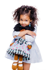 Wall Mural - Portrait of a cute little african american girl hugging doll, isolated on white background