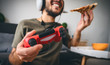© Alessandro Biascioli - Happy man playing online video games while eating pizza fast food - Young gamer having fun on new technology console - Gaming entertainment and youth millennial generation lifestyle concept