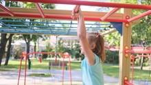 Little Girl Hanging On Monkey Bars In Park On Playground