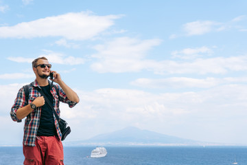 Wall Mural - Male tourist takes the call. Shares impressions and information, uses a smartphone. Communication and mobile internet concept. 5g. View of the sea and Mount Vesuvius. Ocean liner. Copy space