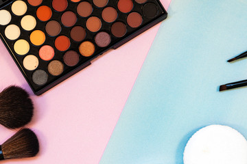 Cosmetics and brushes on a pink-blue background.