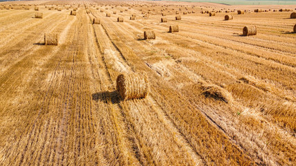 Aerial view at a wide agricultural field with many bales of straw on it.