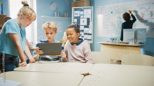 Elementary School Computer Science Class: Two Girls and Boy Use Digital Tablet Computer with Augmented Reality Software, They’re Excited, Full of Wonder, Curiosity. Children in STEM, Playing, Learning