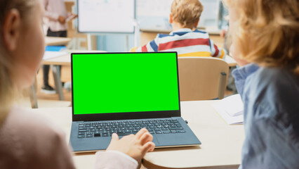 Wall Mural - Elementary School Science Class: Over the Shoulder Little Boy and Girl Use Laptop with Green Screen Mock-up Template on a Display. Physics Teacher Explains Lesson to a Diverse Class full of Smart Kids