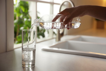 Canvas Print - Woman pouring water from bottle into glass in kitchen, closeup