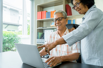 Happy senior Asian couple using a laptop at home for find new tourist attractions together. Happy retirement with planning, saving, pension And the good capital uncle of the elderly