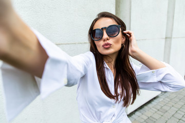 Wall Mural - Young girl take selfie from hands with phone on summer city street. Urban life concept.