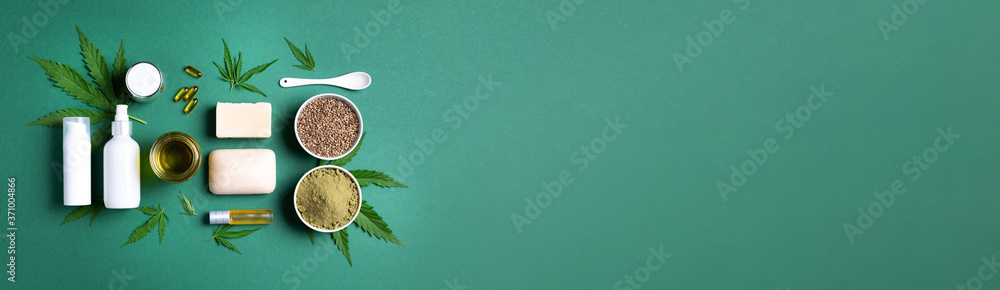 Flat lay with hemp extract products - cosmetics, lotion, face cream, body butter, soap bars, cannabis leaves, seeds, hemp oi, capsules, protein powder, flour on green background. Top view. Banner - obrazy, fototapety, plakaty 