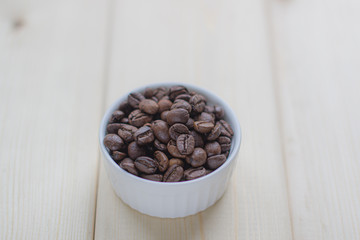Poster - White mug with Cup of coffee beans on wooden background with selective focus and crop fragment