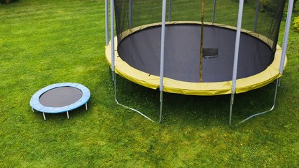 small trampoline near big one with round mat, size comparison, green lawn background