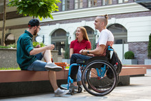 Group Of Friends Taking A Stroll On City's Street In Summer Day. Disabled, Handicapped Man With His Friends Having Fun. Inclusion And Diversity Concept, Normal Lifestyle Of Special Groups Of Society.
