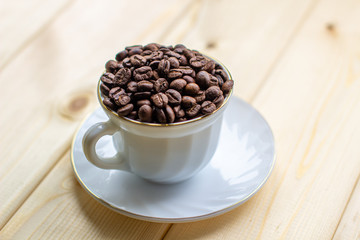 Poster - White mug with Cup of coffee beans on wooden background with selective focus and crop fragment