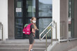 © Natallia - A schoolgirl wearing medical face mask and carrying a pink backpack goes up the stairs of her school, looking back to her parents. Back to school. Protection from virus for school.