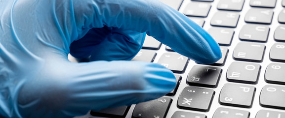 Hands with blue nitrile gloves using a laptop keyboard, performing telework. medical concept. high technologies and computers in medicine