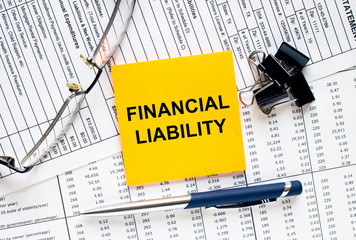 Text Financial Liability on financial tables with pen, glasses and paper clips