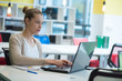 © as-artmedia - Attractive young woman using laptop while sitting at her desk. Young american businesswoman sitting in the office and working on laptop.