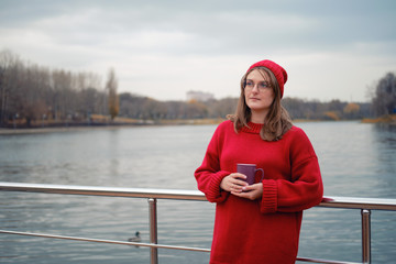 Adult woman by the autumn river with a cup of coffee in her hands, lifestyle