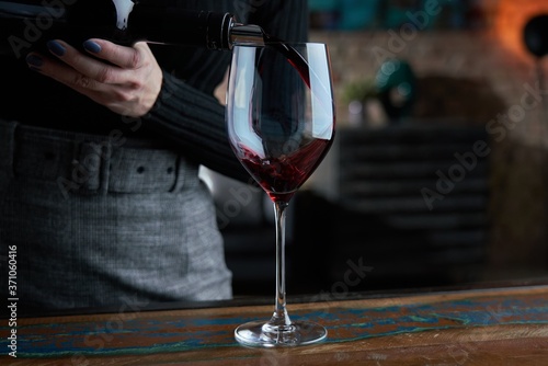 Close up of woman pouring red wine into glass. Dark warm colors.